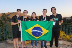 Os cinco estudantes brasileiros medalhistas da 17ª Olimpíada Internacional de Astronomia e Astrofísica segurando a bandeira do Brasil, celebrando a conquista de duas medalhas de prata e três de bronze.